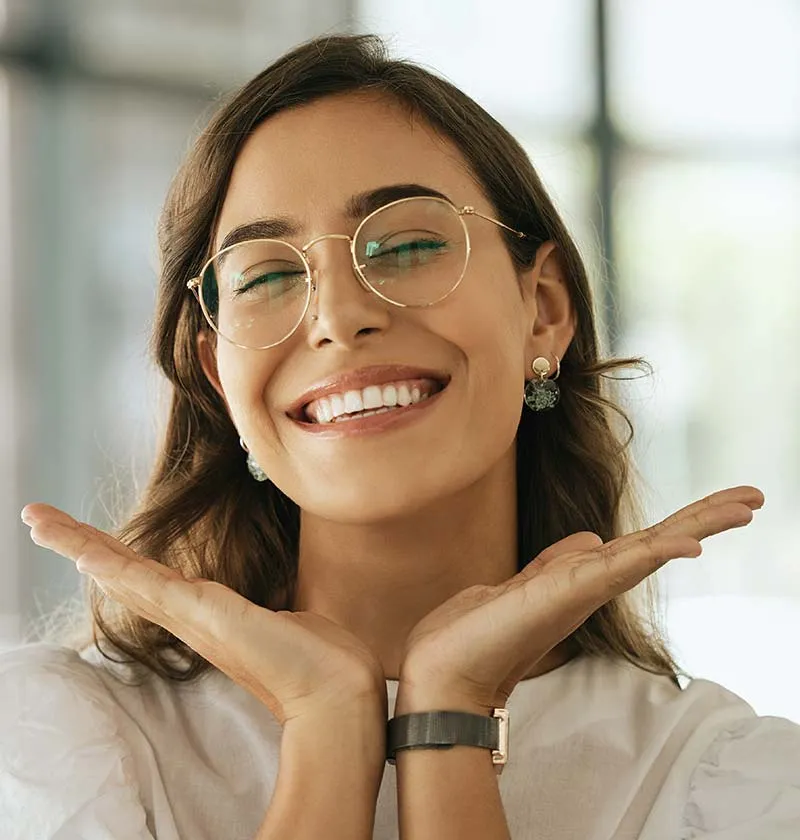 Woman with glasses holding her hands to her chin smiling